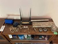 Overview of the lot on a wooden surface including steampunk goggles, calligraphy pens with holder, ink well, whistle, metal scroll holder, pewter cup, cords and metal tools.