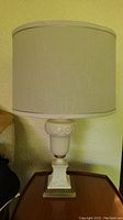 Off-white table lamp with fabric drum shade and decorative carved base on square plinth