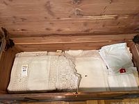 Folded assorted table linens and other linens laid inside a wooden drawer, showing crochet and lace details.