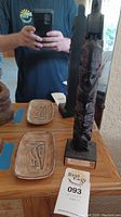 Photo showing 12 inch tall wooden totem pole alongside two rectangular carved wooden dishes on a wooden surface.