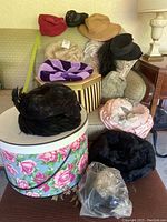 Photo showing assortment of vintage hats on couch and two hat boxes