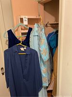 Photo of women's dresses including navy long-sleeve dress, blue velvet dress, light blue embroidered dress on hangers