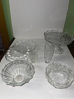 Overall view of the lot showing various clear glass bowls, cake stands, and a vase on a white surface.