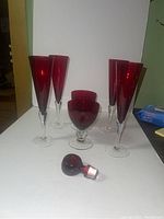 All four ruby red champagne flutes, two ruby red goblets, and one ruby red glass stopper laid out on a white surface