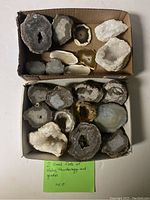 Two small flats containing assorted slabs, thundereggs, and geodes viewed from above, showing a collection of natural stones with varied textures and colors.
