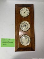 Front view of the weather station with all three dials visible: hygrometer, barometer, thermometer in wooden frame