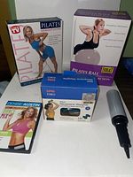 Photo of boxed Pilates workout system, Everlast Pilates ball with box, boxed neoprene weights, Denise Austin dance mix DVD, and air pump on white surface