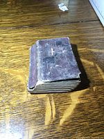 Small, worn, and aged pocket book placed on a wooden surface, showing wear on the spine and cover.
