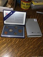 Overview photo of the 1990 coin set in its original blue presentation case and its silver slipcase, showing all six coins and informational booklet in the lid.