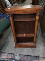 Front view of the antique solid wood clock case repurposed display shelf showing the rectangular top, two shelves, turned column supports, and base.
