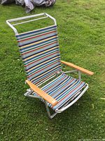 Photo of reclining beach chair with aluminum frame and wood arms on grass, showing angled view and striped fabric seating