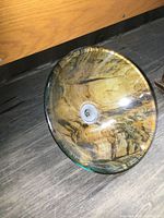 Glass bowl sink with brown and gold swirling pattern inside, round with a central drain fitted. Shown on a floor with light reflection on the glossy surface.