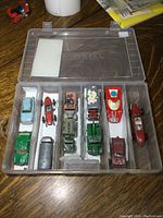 Plastic storage case with 11 assorted diecast cars separated by compartments, showing variety of colors and models.