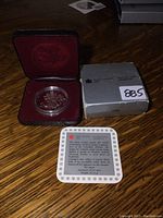 Silver dollar displayed in the open red velvet presentation case alongside the original gray box and certificate of authenticity on a wooden surface.