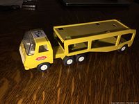 Side-right angle view of the vintage yellow Tonka pressed steel truck and car carrier trailer showing the cab and the two-level open trailer design with wheels and Tonka logos.