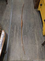 Full-length view of the vintage wooden bow on the wooden floor showing the gently curved shape and full length.