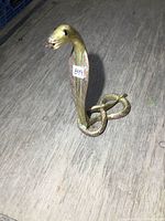 Brass cobra snake figurine standing on wooden surface, showing front and side views with visible tag '899'