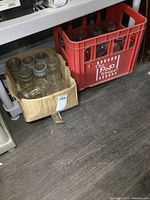 Cardboard box and red plastic crate holding a number of vintage glass canning jars with metal rings and glass lids.