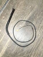 Full length of black woven leather whip laid out on wooden surface.