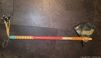 Full view of the hatchet showing the entire length with wooden handle decorated with red and tan bands and bead-end hanging loops.