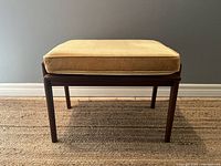Front view of mid century modern teak footstool with mustard yellow removable cushion on top