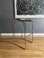 Front angle view showing the high stool with chrome seat and frame against a gray wall and wood floor.