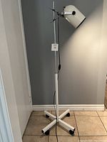 Full view of white and chrome post-modern floor lamp standing on tiled floor.