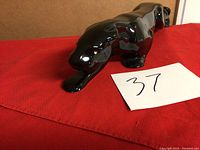 Black glossy ceramic panther figurine shown from side angle on red cloth, crouching pose