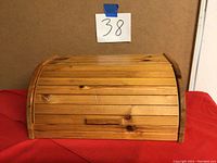 Front view of wooden bread box with roll-top slatted lid showing surface scratches and rounded edges.