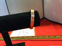Copper bracelet displayed on black stand with measuring tape showing diameter approximately 6.5 inches