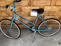 Side view of blue 1985 Fuji 5-speed bike with flat tires, showing frame, pedals, chain, and kickstand.