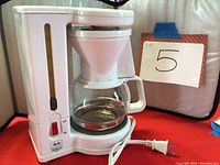 Front view of the white Gevalia coffee maker showing on/off switch, water level indicator, glass carafe on warming plate.