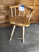 Solid wood swivel chair front view showing natural wood finish, contoured seat, and spindle backrest with item tag 23 on top rail.