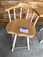 Front view of a solid wood swivel chair with white legs and brass footrest, showing marked wood and turned spindles.