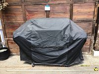 Outdoor grill fully covered by a black grill cover, showing size and shape of covered grill.