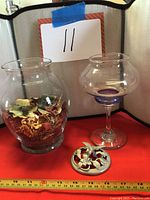 Two clear glass potpourri containers, one filled with dried potpourri and one topped with a pewter hummingbird lid beside it.