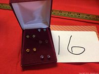 Photo of five pairs of stud earrings with different colored gemstones displayed in a velvet-lined jewelry box.