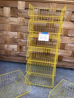 Stack of six yellow wire baskets with two larger yellow wire baskets on the ground in front, some baskets show damage or need ties to secure.