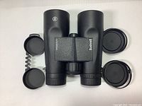 Top-down view of black Bushnell binoculars showing front lenses and attached lens covers.