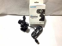 Webcam with USB cable coiled next to retail box showing front of packaging with Safari branding and product info.