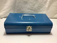 Closed blue metal toolbox with silver handle and front latch, visible wear and paint marks.