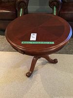 Full view of round wooden end table showing the sunburst veneer tabletop and carved tripod pedestal base with scroll feet.