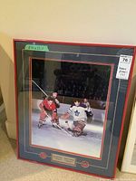 Framed hockey photograph showing Jean Beliveau in Montreal Canadiens jersey and Johnny Bower in Toronto Maple Leafs jersey on ice with visible plaque and medallions
