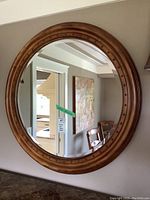 Full view of the round mirror showing the wooden frame with nailhead decorative elements and clear reflective surface.
