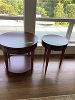 Two round wooden end tables of different sizes placed near glass doors, showing overall condition and size difference.