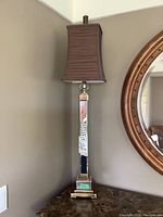Full view of one tall lamp showing brown fabric shade and mirrored column with brass accents.