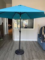 Full view of blue patio umbrella open and standing indoors on floor