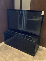 Full view of Samsung plasma TV on black TV stand with Samsung sound bar on stand shelf