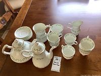 Full tea set displayed on wooden table including tea pot, coffee pot, 6 cups and saucers, cream and sugar bowl.