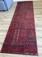 Full view of long red runner rug laid on light wooden floor showing overall design and pattern.